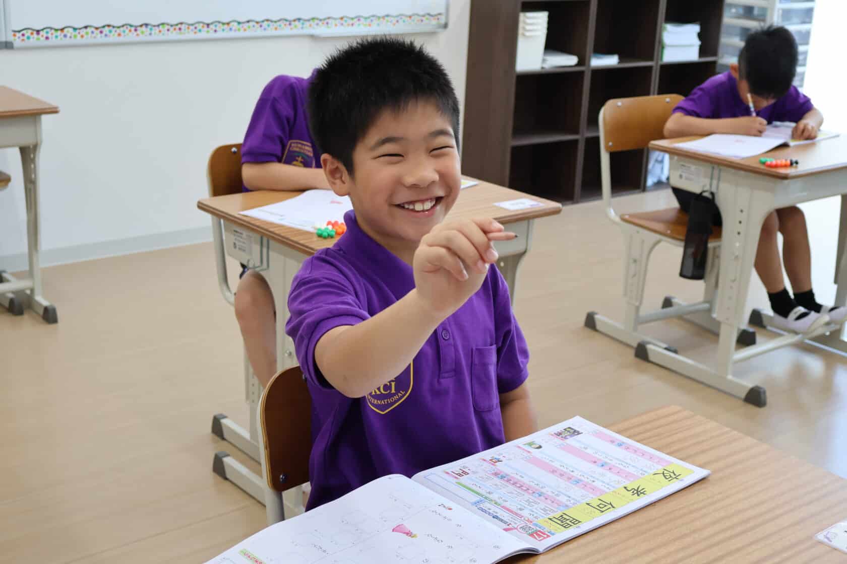 KCIの教室内で、教科書とワークブックを使って集中して国語（日本語）の勉強に取り組む小学2年生の男の子の様子。