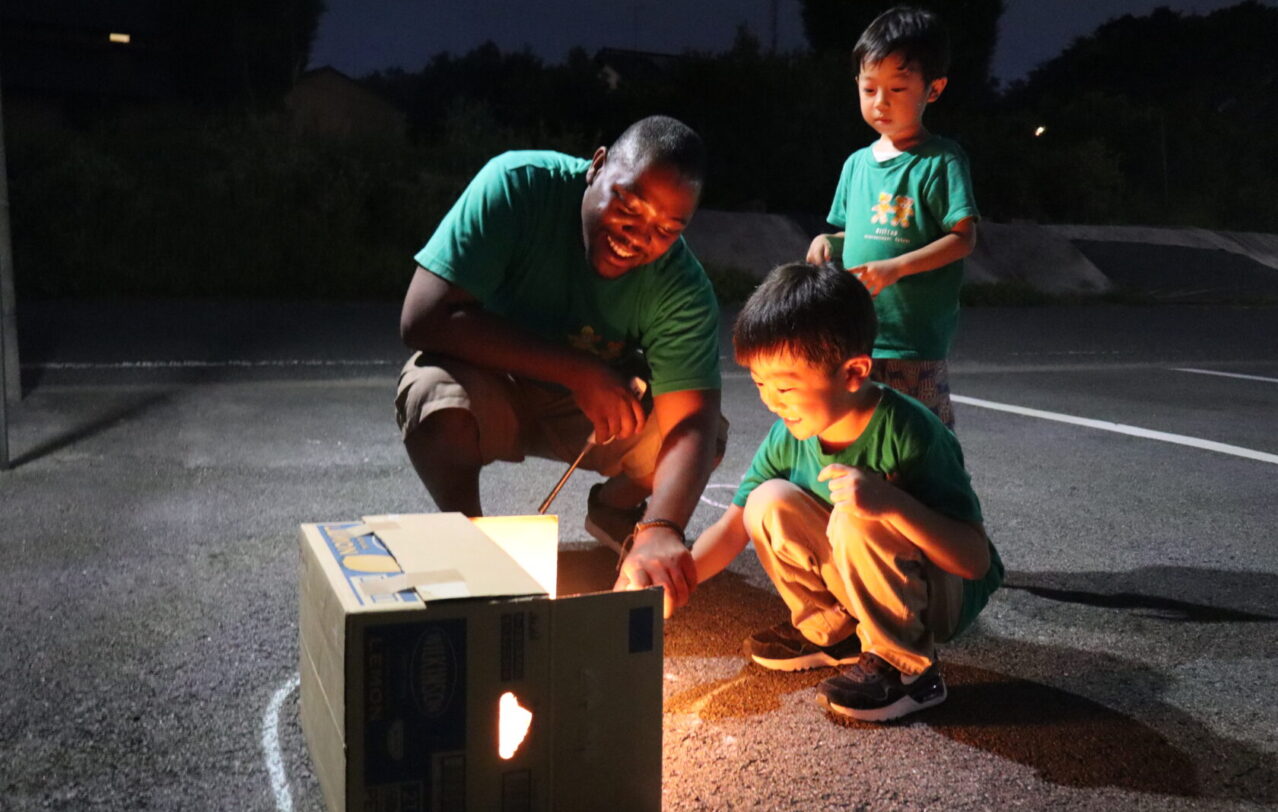 A child lighting a sparkler with a teacher during Summer Camp at Hilltop International School in Kumamoto, Japan.熊本市のヒルトップインターナショナルスクールのサマーキャンプで、先生と一緒に花火を楽しむ園児。