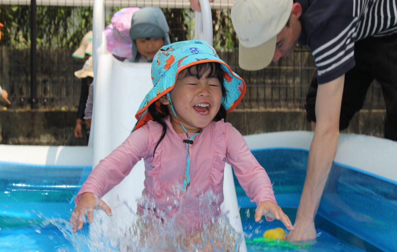 A child sliding into a kiddie pool during Water Play at Hilltop International School in Kumamoto, Japan.熊本市のヒルトップインターナショナルスクールで水遊びを楽しむ園児　