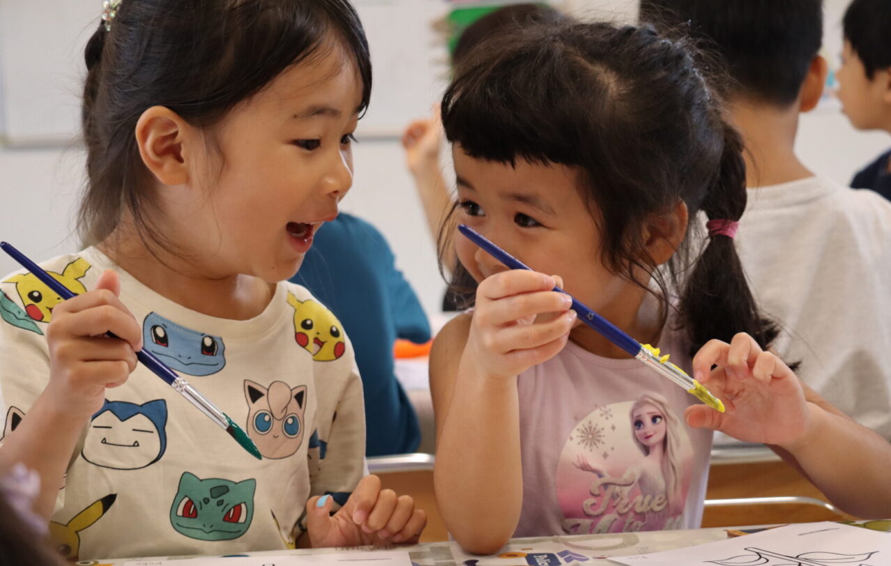 Two girls in Lion Class painting together during an art activity at Hilltop International School in Kumamoto, Japan. 熊本市のヒルトップインターナショナルスクールで、アート活動として一緒に絵を描くLionクラスの2人の女の子。