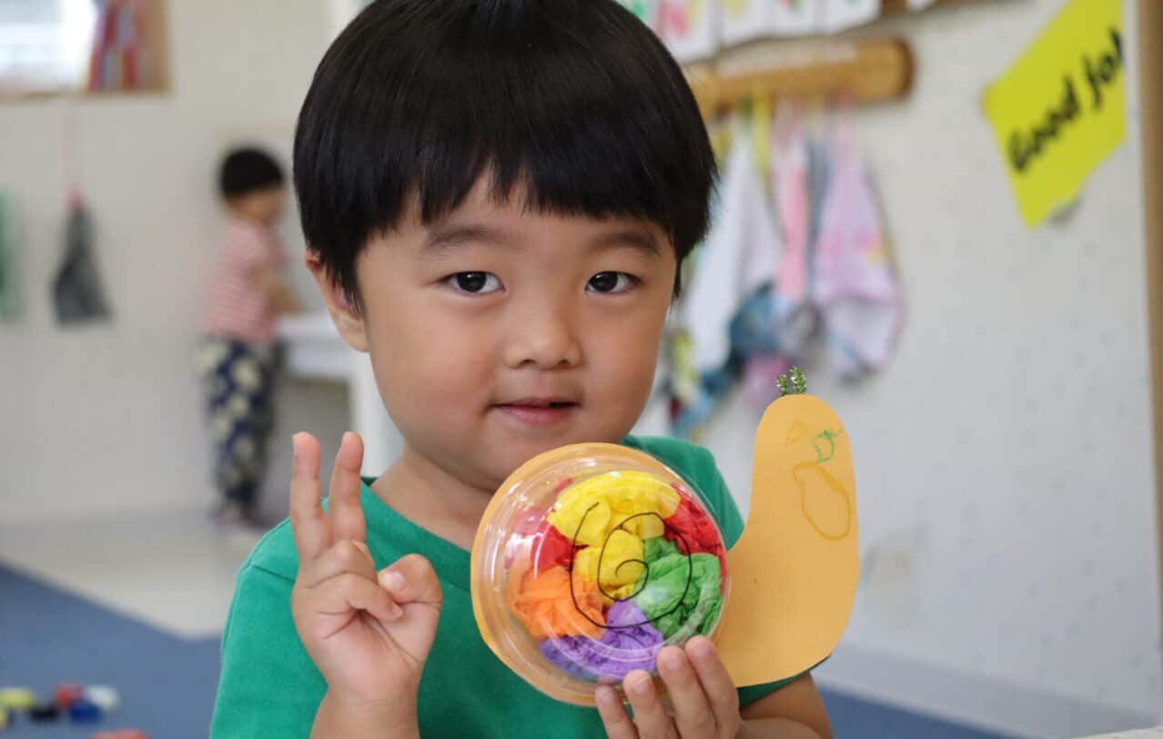 熊本のヒルトップインターナショナルスクールで、手作りのカタツムリの工作を持つ生徒。A student proudly holding up a handmade snail craft at Hilltop International School in Kumamoto.